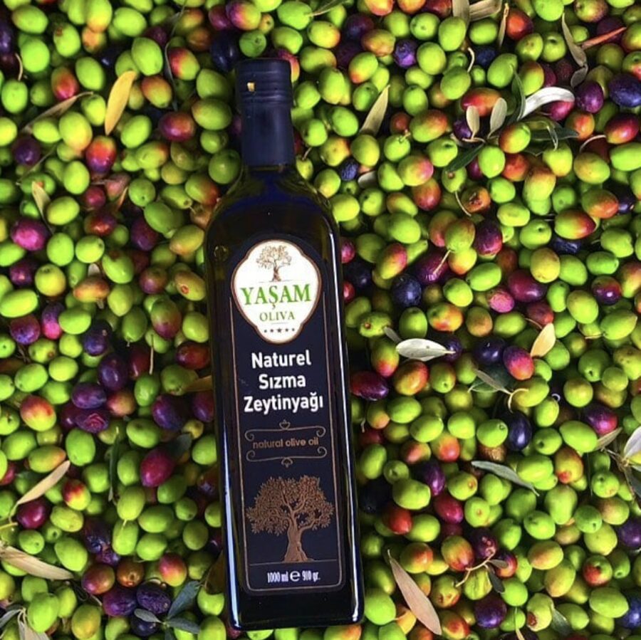 Toplanmış yeşil ve siyah zeytinlerin üzerinde duran Yaşam Oliva naturel sızma zeytinyağı şişesi