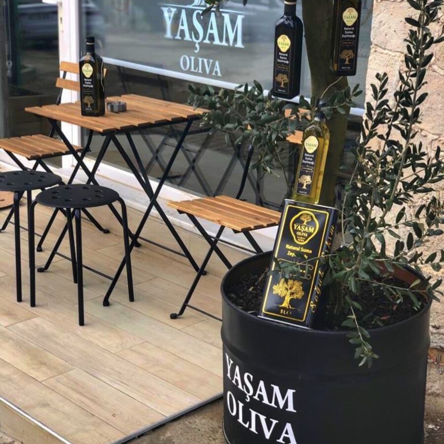 Yaşam Oliva dükkânının önündeki ahşap masalar ve vitrindeki zeytinyağı şişeleri